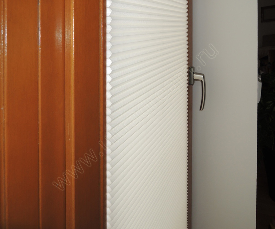 Белые шторы плиссе со встроенным электроприводом установлены на дверях с остеклением